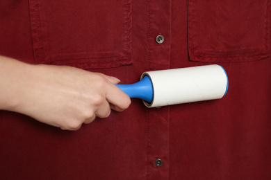 Photo of Woman cleaning red shirt with lint roller, closeup