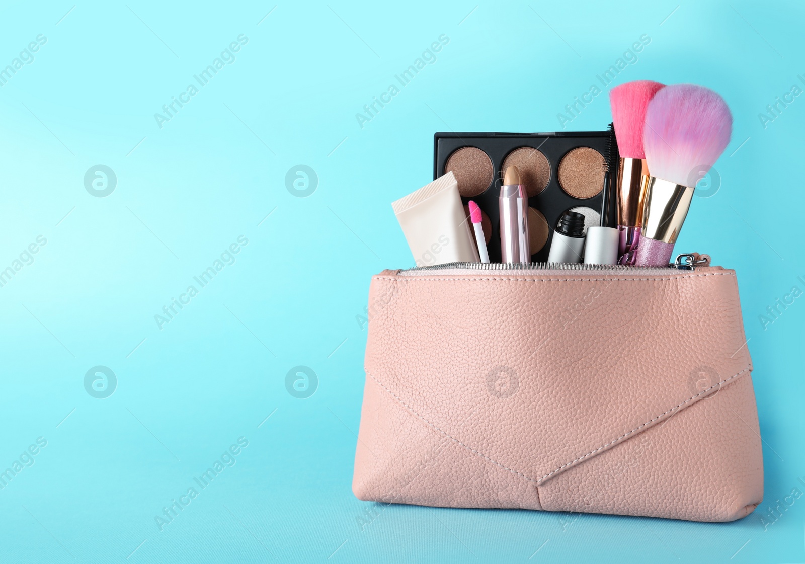 Photo of Cosmetic bag with makeup products and accessories on light blue background. Space for text