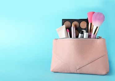 Photo of Cosmetic bag with makeup products and accessories on light blue background. Space for text