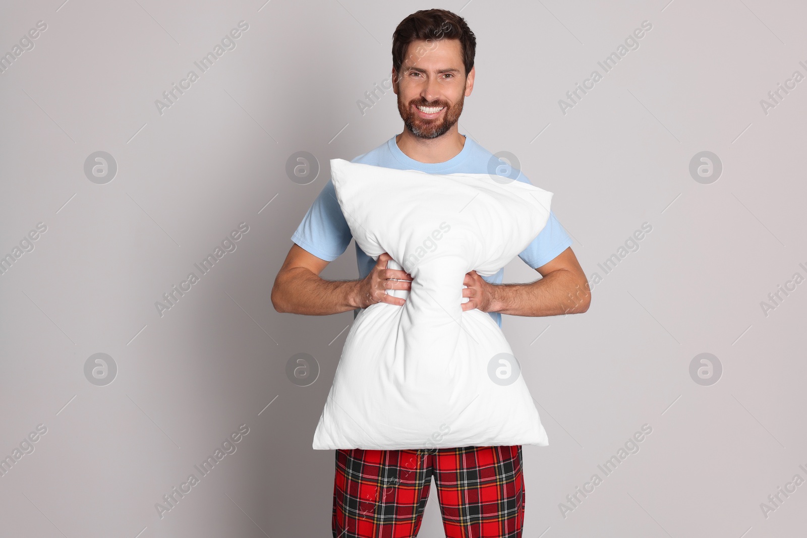 Photo of Smiling handsome man with soft pillow on light grey background