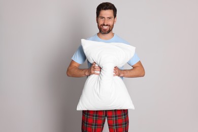 Smiling handsome man with soft pillow on light grey background