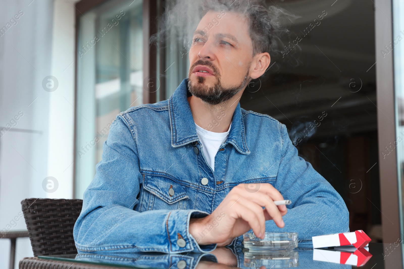 Photo of Handsome man smoking cigarette at table in outdoor cafe