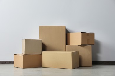 Photo of Many closed cardboard boxes on floor near white wall. Delivery service