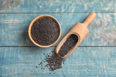 Bowl and scoop with uncooked black rice on blue wooden background, top view