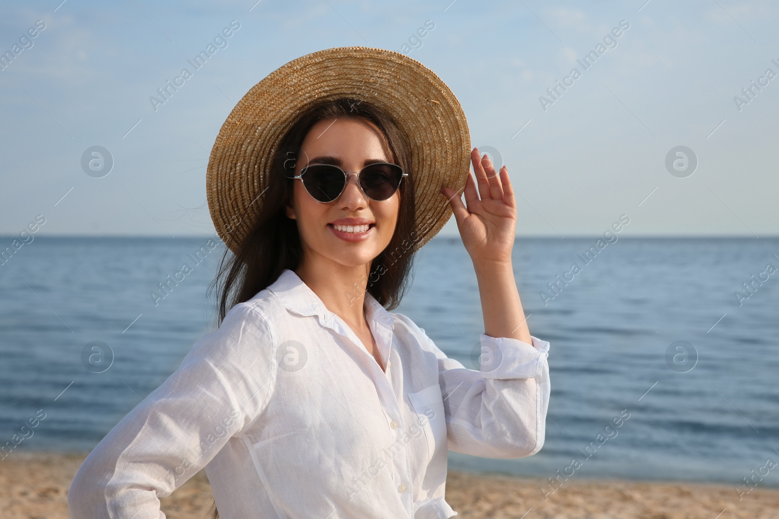 Photo of Beautiful young woman wearing straw hat and sunglasses on beach. Stylish headdress