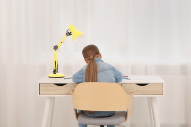 Photo of Girl sitting at desk in room, back view. Home workplace