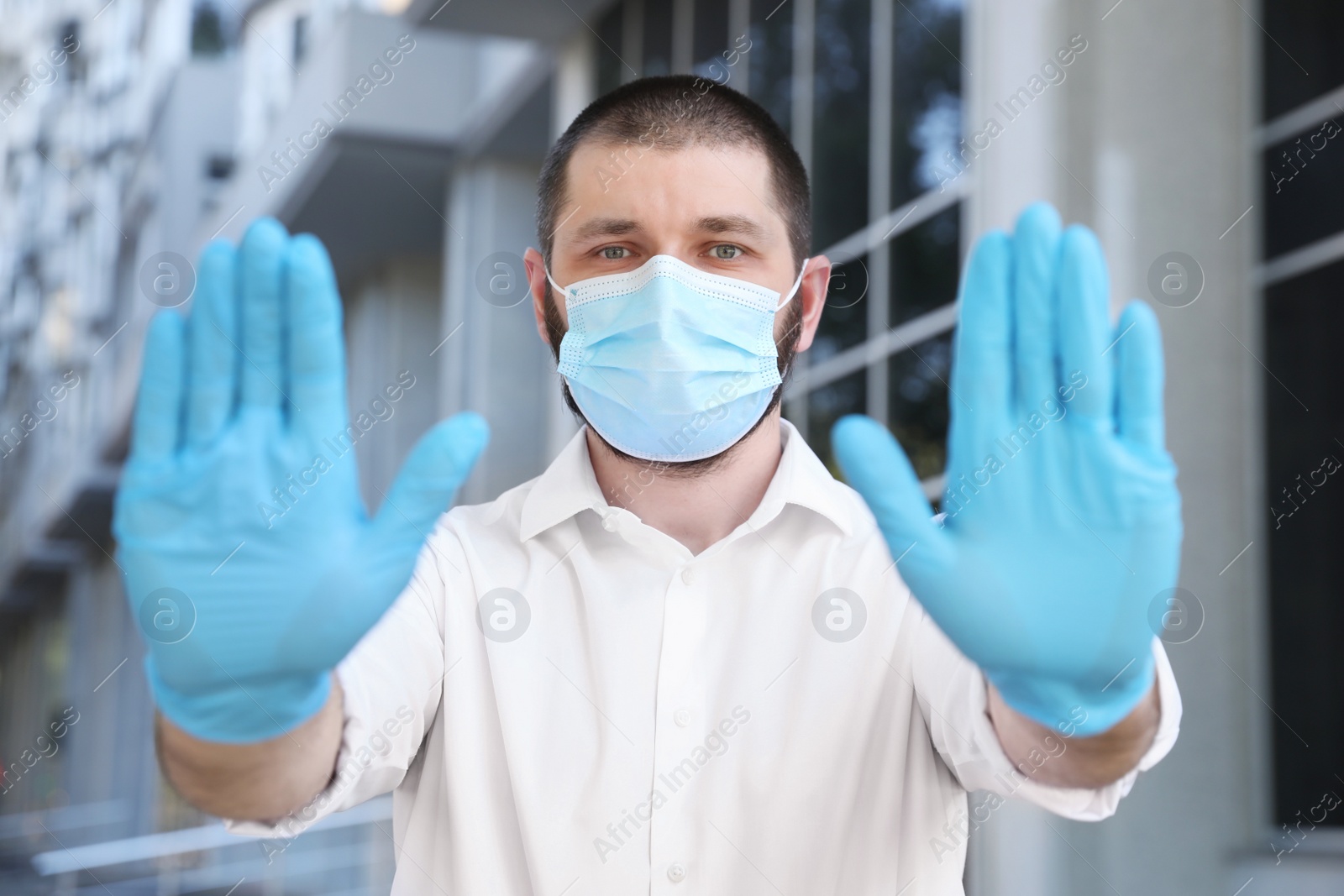 Photo of Man in protective face mask showing stop gesture outdoors. Prevent spreading of coronavirus