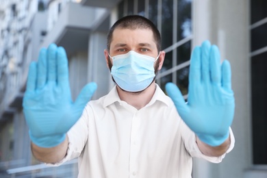 Man in protective face mask showing stop gesture outdoors. Prevent spreading of coronavirus
