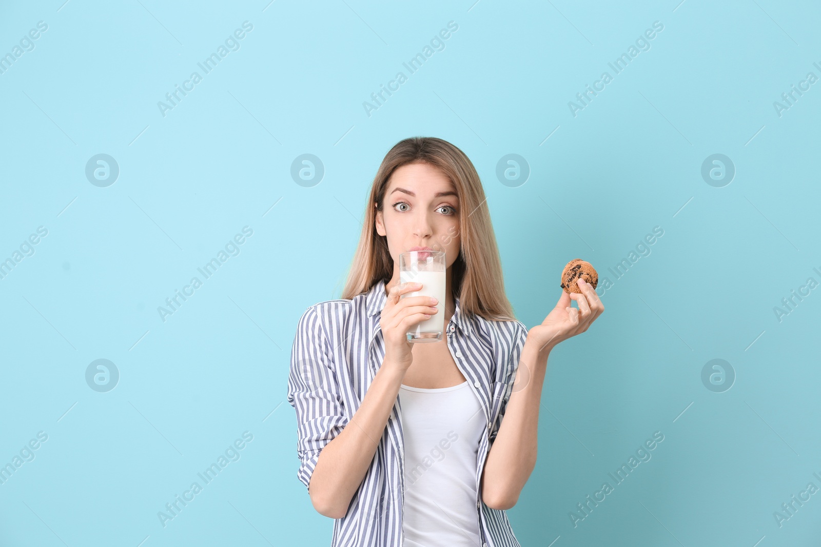 Photo of Beautiful young woman drinking milk with cookies on color background