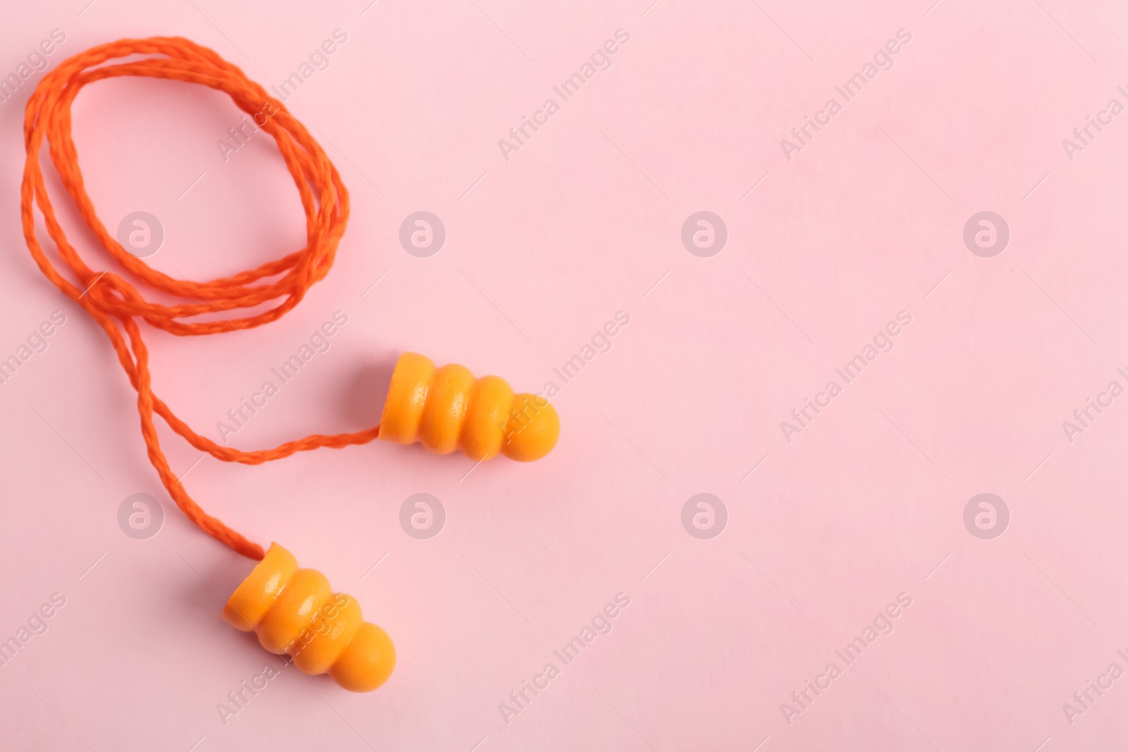 Photo of Pair of orange ear plugs with cord on pink background, top view. Space for text