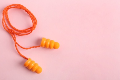 Pair of orange ear plugs with cord on pink background, top view. Space for text
