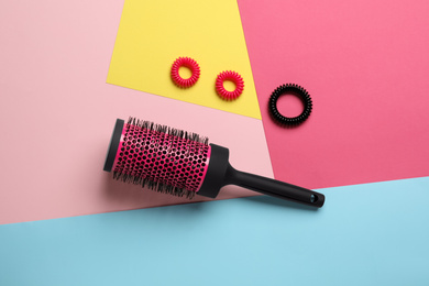 Round hair brush and scrunchies on color background, flat lay