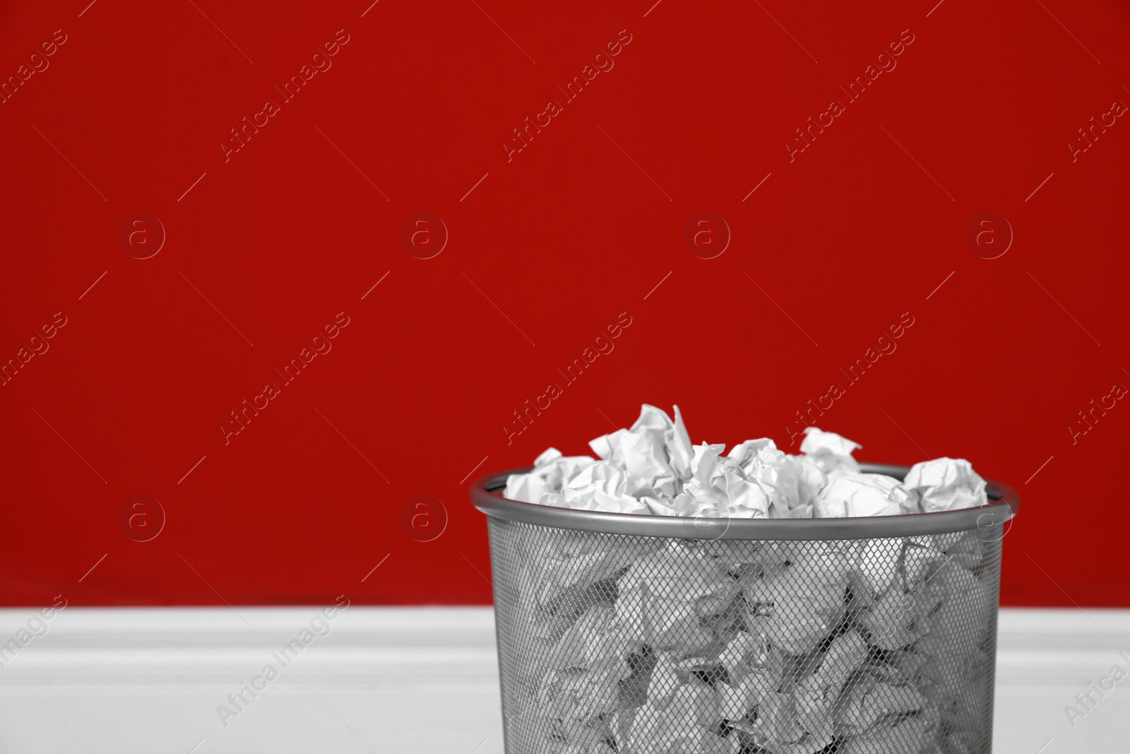 Photo of Metal bin with crumpled paper against color wall, closeup. Space for text