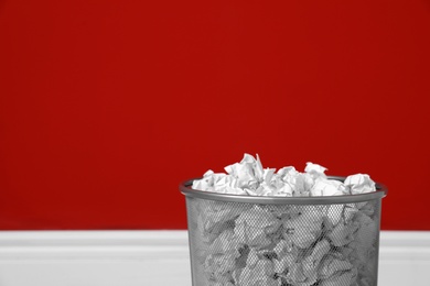 Photo of Metal bin with crumpled paper against color wall, closeup. Space for text