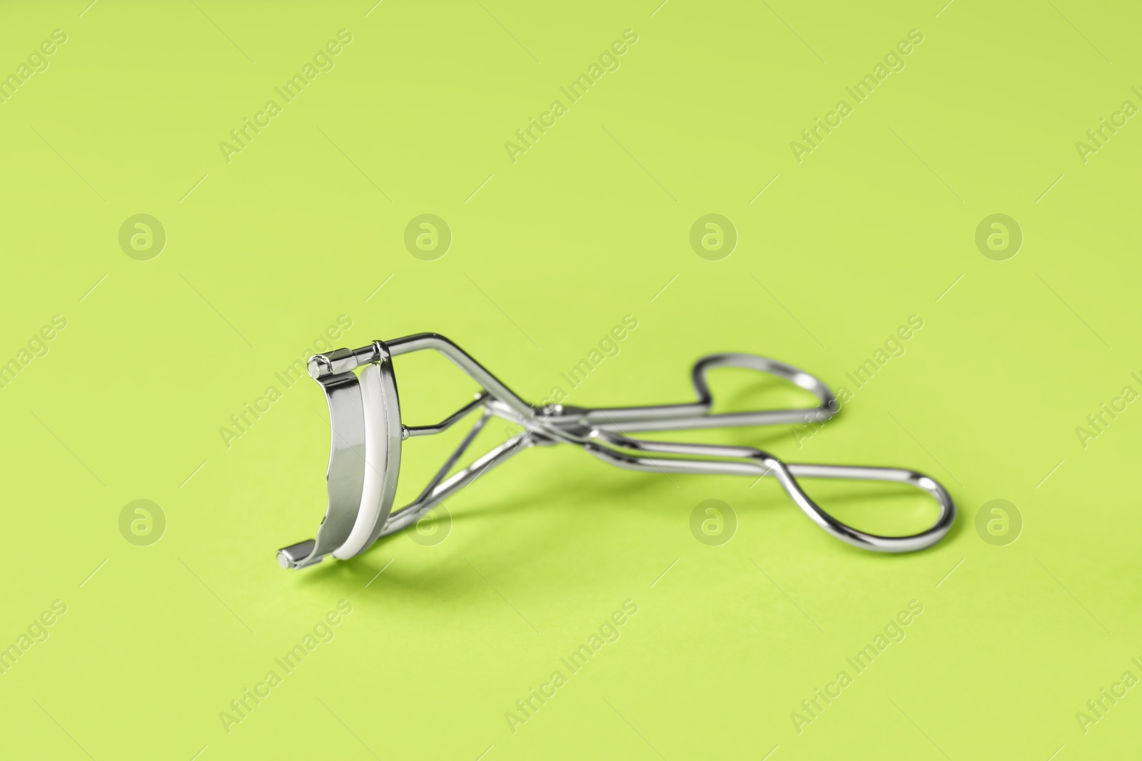 Photo of Eyelash curler on light green background. Makeup tool