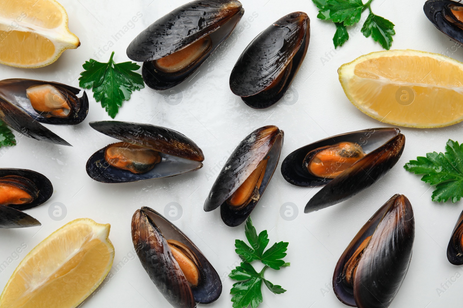 Photo of Cooked mussels with parsley and lemon on white marble table, flat lay