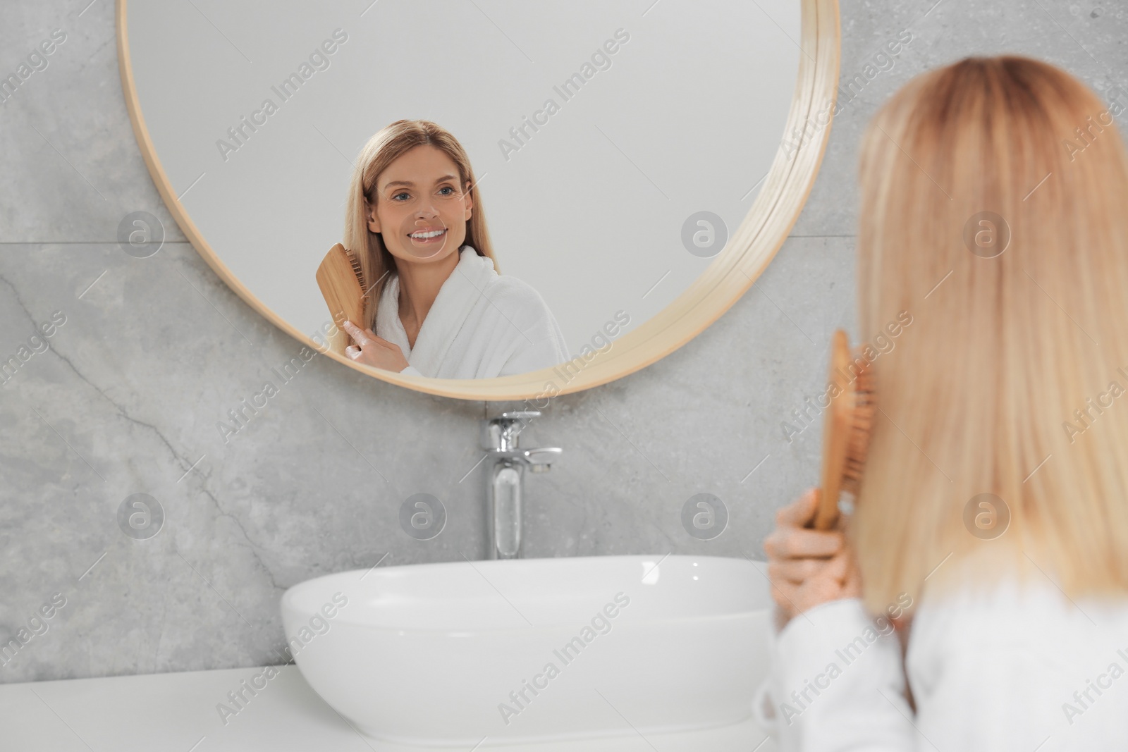 Photo of Beautiful woman brushing her hair near mirror in bathroom