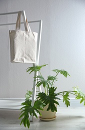 Photo of Houseplant and eco bag on rack near white wall. Space for design