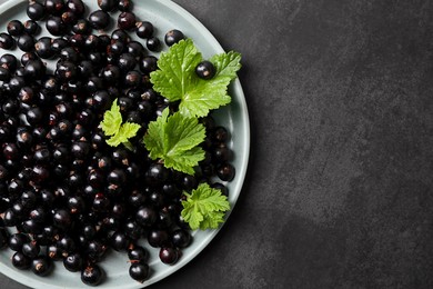 Photo of Plate with ripe blackcurrants and leaves on grey background, top view. Space for text