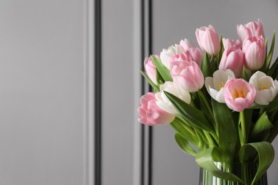 Beautiful bouquet of tulips in glass vase against grey wall. Space for text