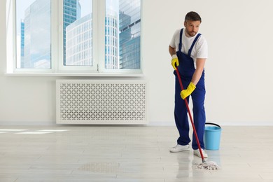 Man in uniform cleaning floor with mop indoors. Space for text