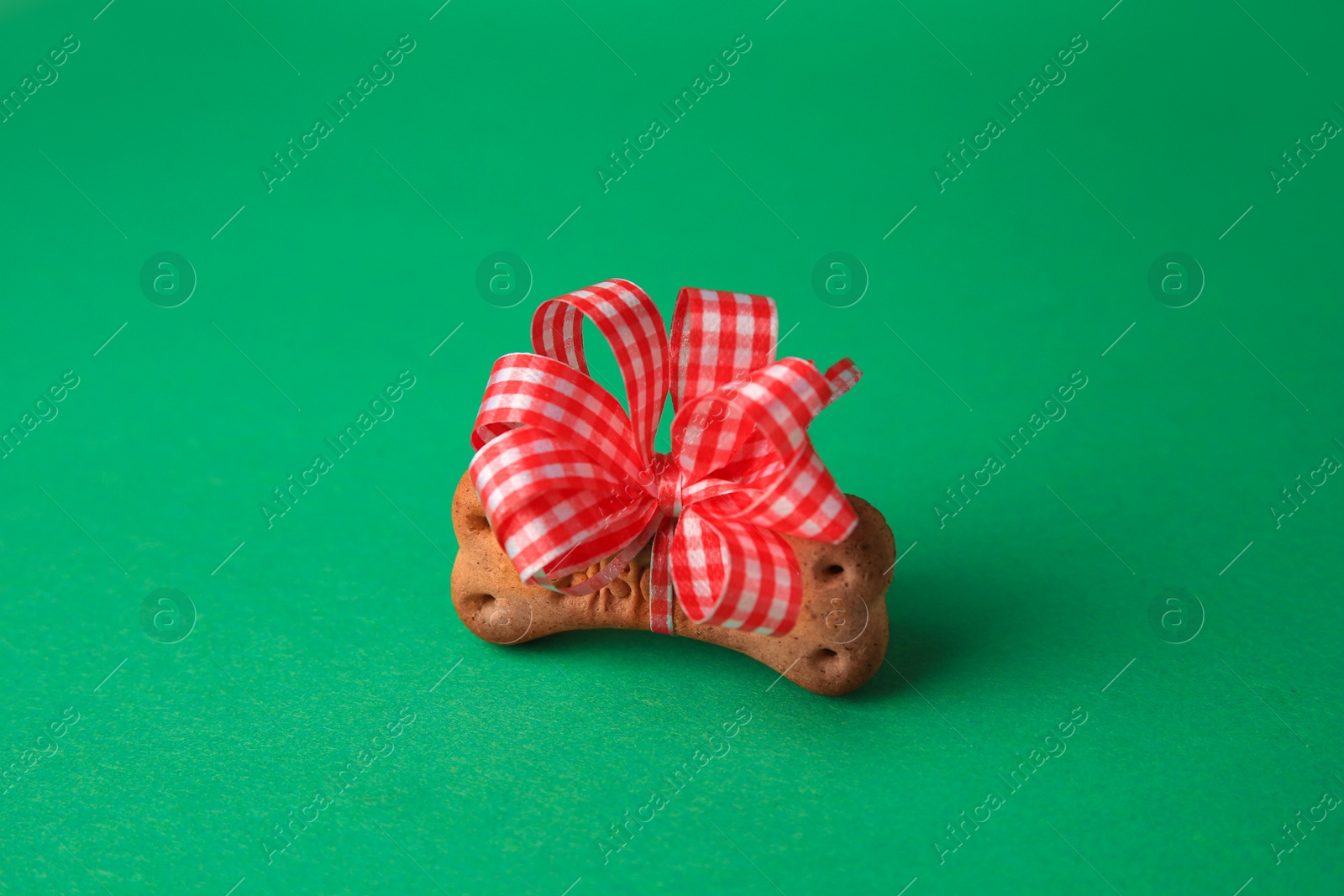 Photo of Bone shaped dog cookie with red bow on green background