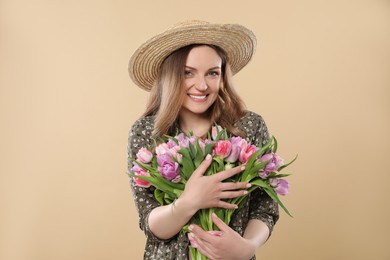 Photo of Happy young woman in straw hat holding bouquet of beautiful tulips on beige background