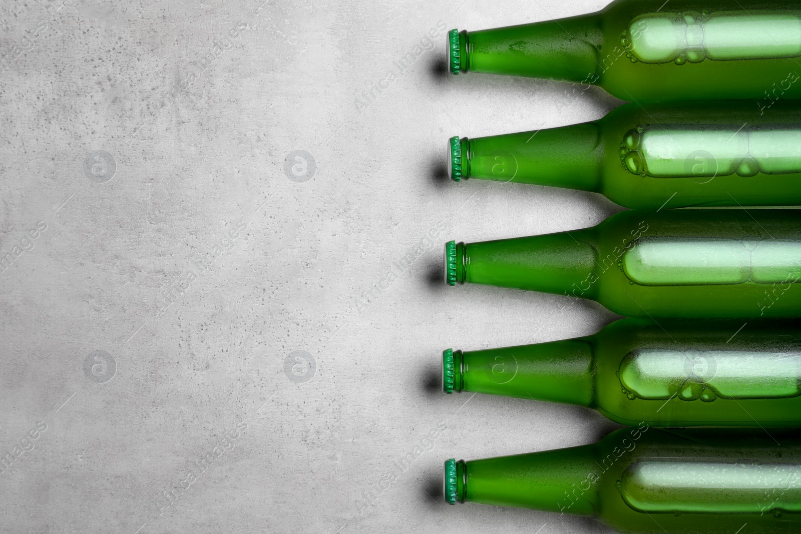 Photo of Glass bottles of beer on light grey background, flat lay. Space for text