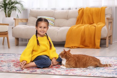 Photo of Happy little girl and cute ginger cat on carpet at home