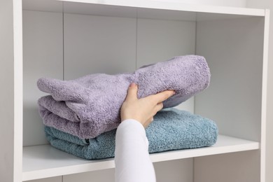 Photo of Woman stacking clean towels on shelf indoors, closeup