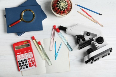 Photo of Laboratory glassware, microscope and school supplies on wooden background, flat lay