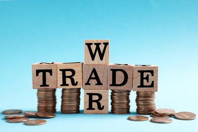 Photo of Wooden cubes with phrase Trade war and coins on light blue background