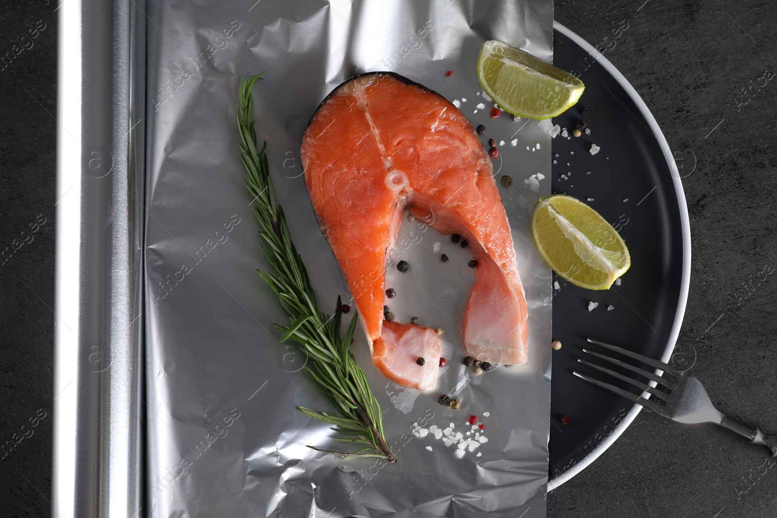 Photo of Aluminum foil with raw fish, lime, rosemary and spices on grey textured table, flat lay. Baking salmon