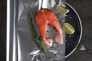 Aluminum foil with raw fish, lime, rosemary and spices on grey textured table, flat lay. Baking salmon