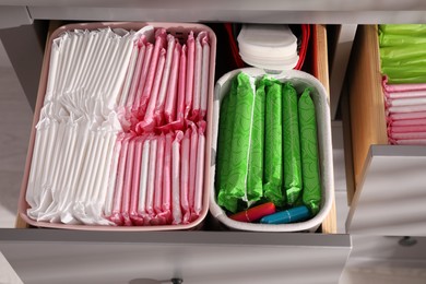 Photo of Open cabinet drawers with menstrual pads, tampons and pantyliners indoors, above view