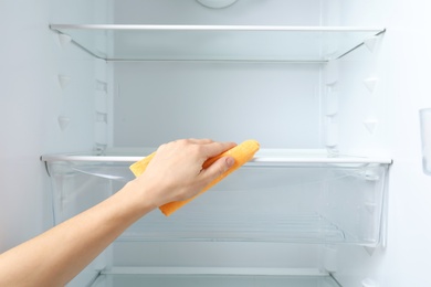 Photo of Woman cleaning empty refrigerator with rag, closeup