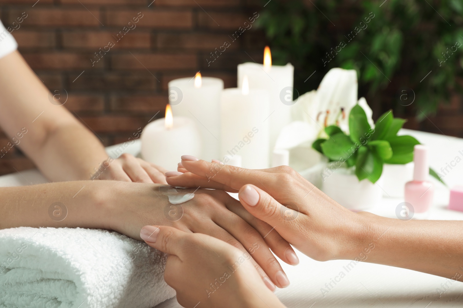 Photo of Cosmetologist applying cream on woman's hand at table in spa salon, closeup with space for text