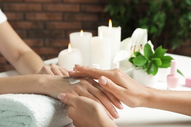 Cosmetologist applying cream on woman's hand at table in spa salon, closeup with space for text