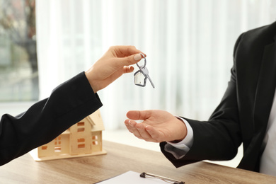 Photo of Real estate agent giving key to client at table in office, closeup