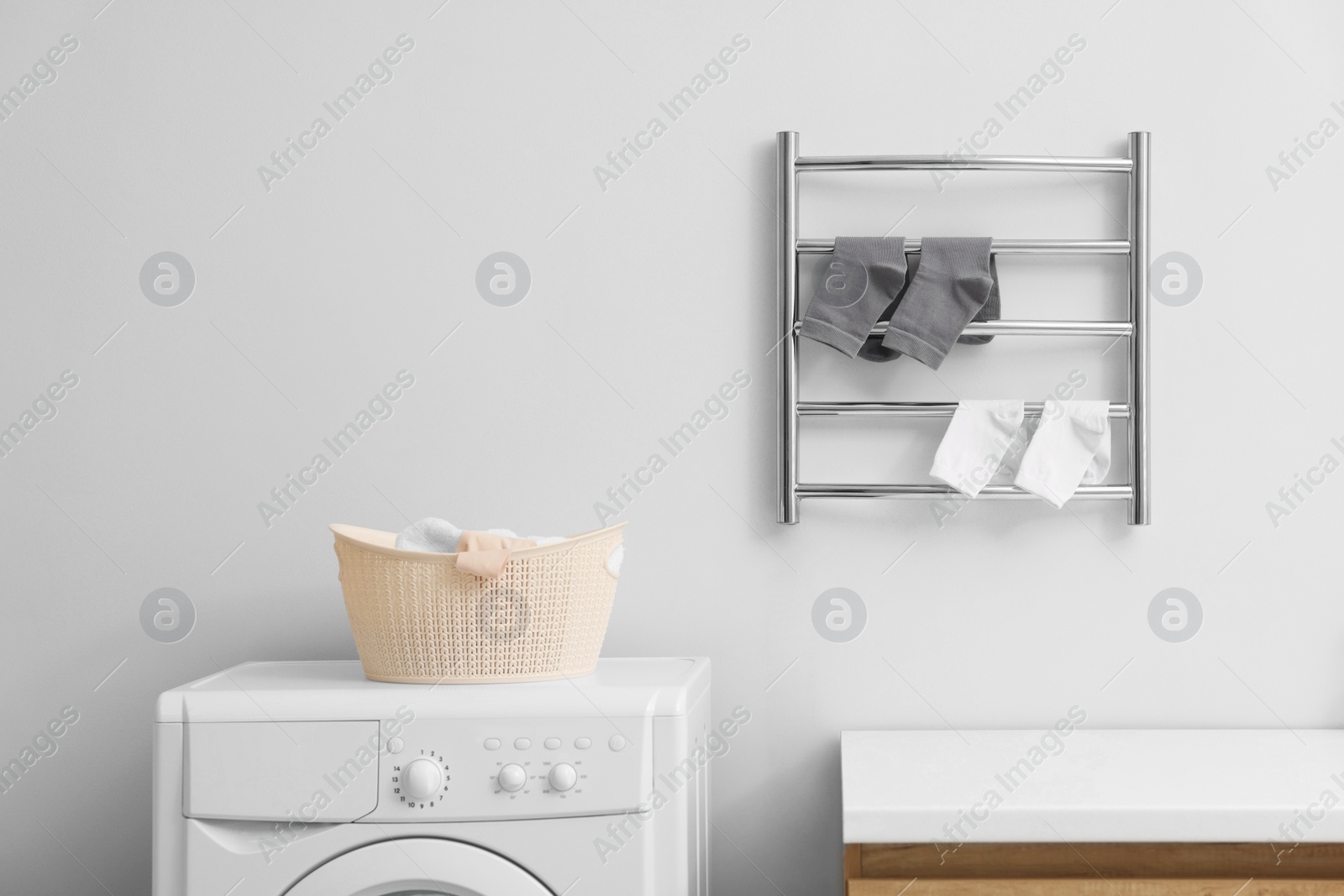 Photo of Heated towel rail with socks on white wall in bathroom, space for text