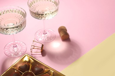Photo of Glasses of expensive white wine, cork and heart shaped chocolate candies on color background. Space for text