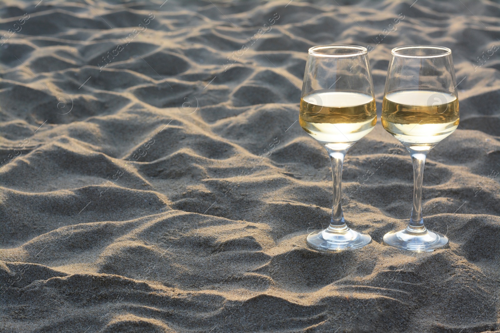 Photo of Glasses of tasty wine on sand, space for text