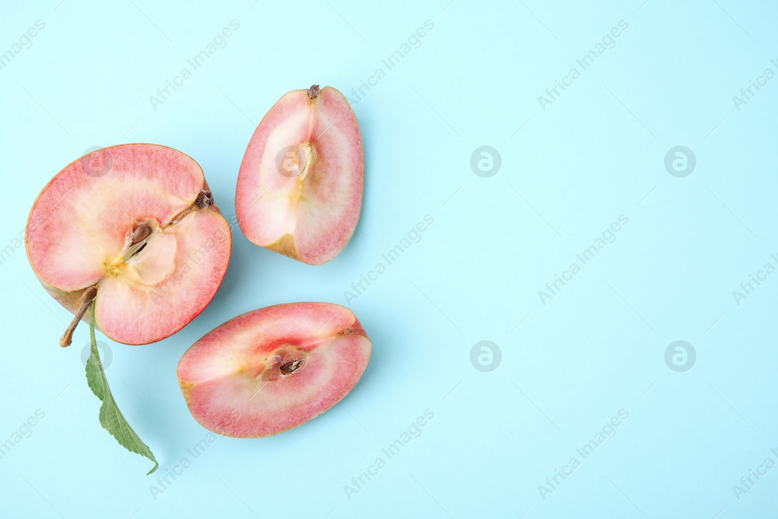Photo of Cut apple with red pulp on light blue background, flat lay. Space for text