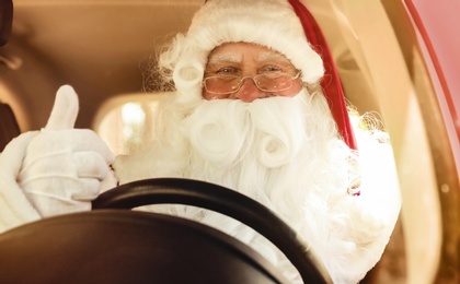 Photo of Authentic Santa Claus driving modern car with fir tree, view through windshield