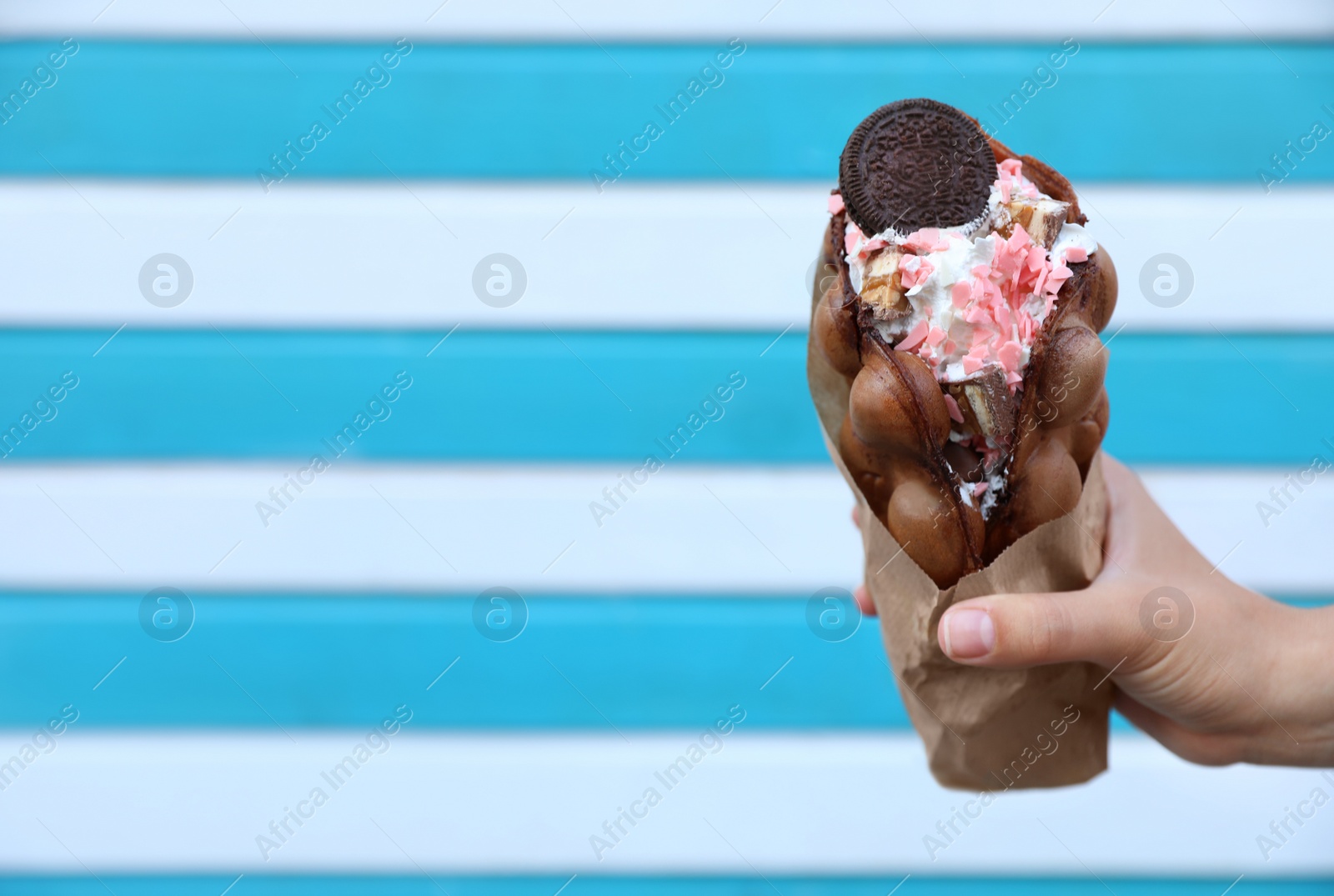 Photo of Young woman holding delicious sweet bubble waffle with ice cream on color background, closeup. Space for text