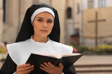 Photo of Young nun reading Bible outdoors, space for text