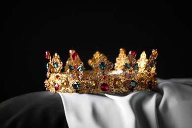 Beautiful gold crown with gems on pillow against black background