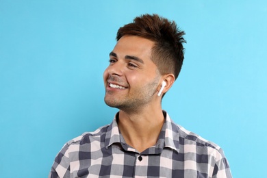 Happy young man listening to music through wireless earphones on light blue background