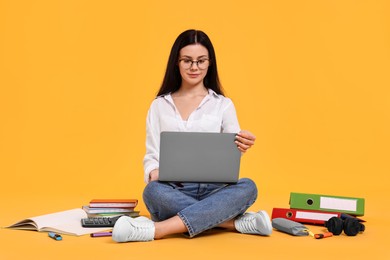 Student with laptop sitting among books and stationery on yellow background