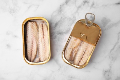 Open tin cans with mackerel fillets on white marble table, flat lay